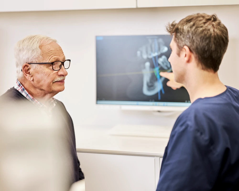 Dr. Kalkreuter und Patient betrachten gemeinsam die navigierte 3D-Implantation am Monitor.