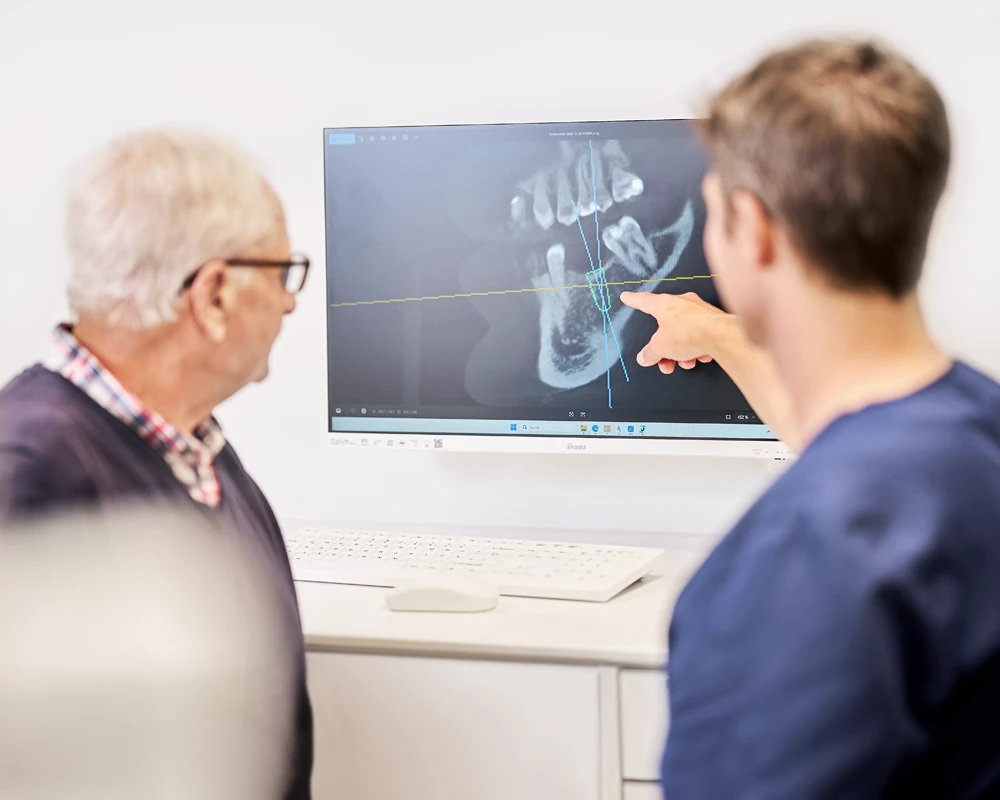 Behandlungsgespräch: Dr. Kalkreuter erläutert einem Patienten die 3D-Implantatplanung am Monitor.