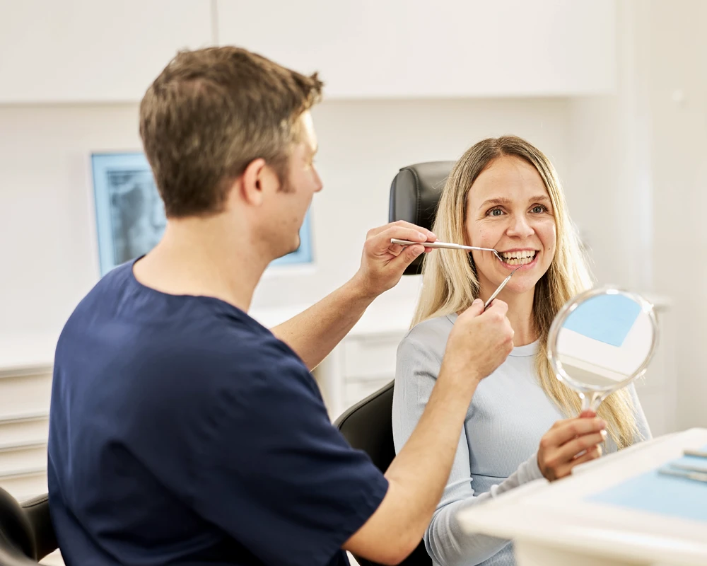 Dr. Kalkreuter bespricht mit Patientin regenerative Therapie und zeigt ihr mit Hilfe eine Handspiegels die Thematik an ihren Zähnen.